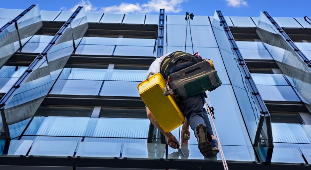 Profissional de manutenção predial suspenso por cordas realizando limpeza e reparo em fachada de vidro de um edifício moderno." (O Google usa isso para entender que a Lumina lida com serviços de manutenção e conservação).