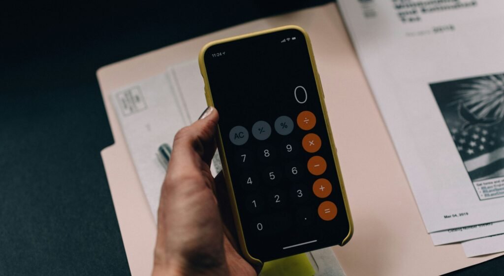 Pessoa segurando smartphone com aplicativo de calculadora aberto sobre pastas de documentos e relatórios financeiros de um condomínio.